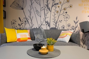 A modern living room with a grey sofa, colorful cushions, a black bowl, a yellow candle, and a potted plant on a woven mat. - IMCT - Dockhouse Soho 2 (Budapest)