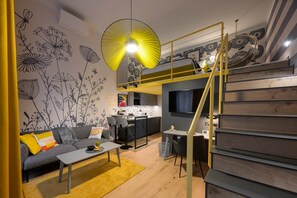 A modern interior with a sofa, coffee table, and a dining area with chairs. There is a kitchen with a TV above the counter. - IMCT - Dockhouse Soho 2 (Budapest)