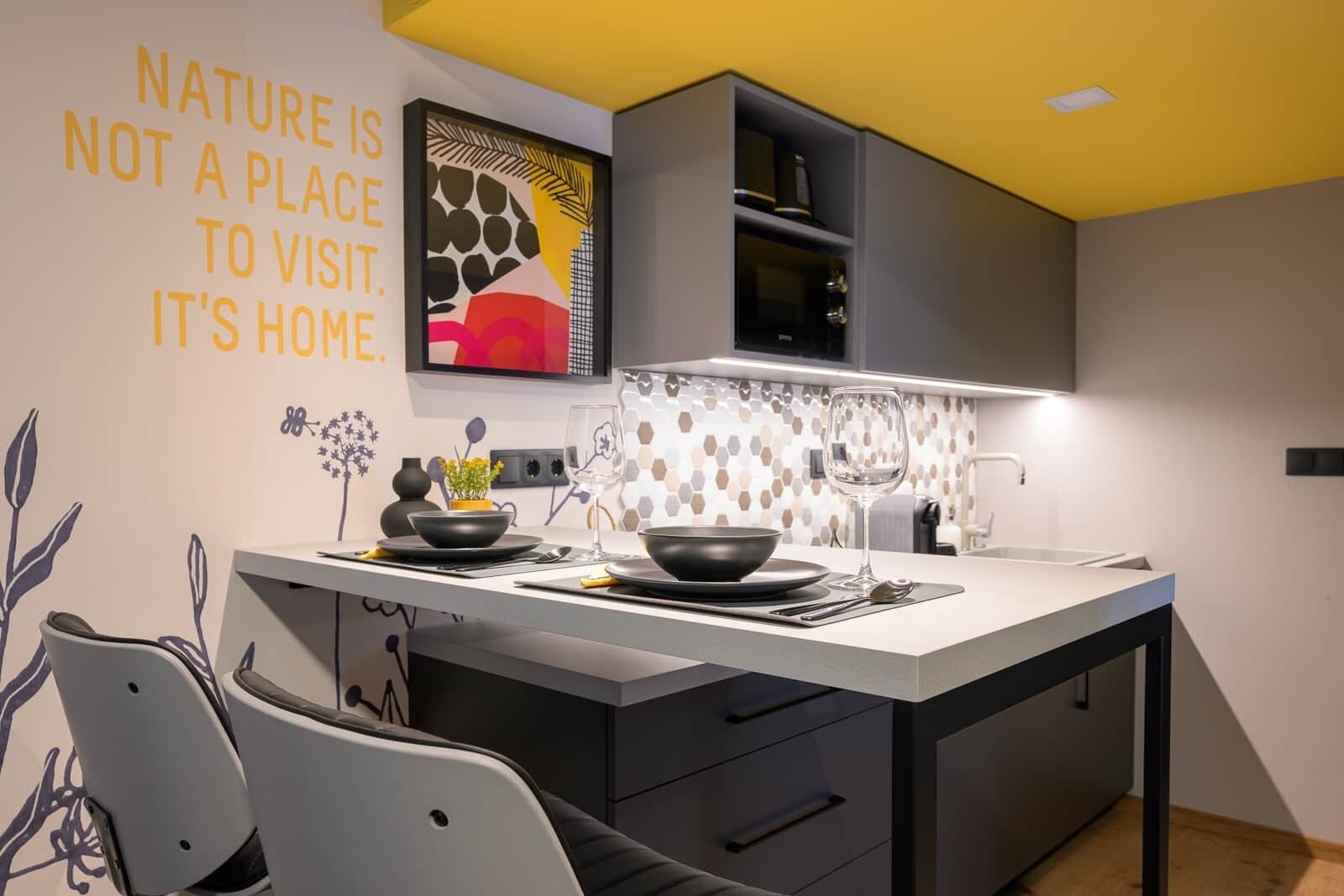 A modern kitchen with a central island, black cabinets, and a decorative wall with a nature-themed artwork.