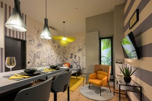 A modern living room with a dining area, featuring a sofa, chairs, a TV, and a decorative wall with a floral pattern. - IMCT - Dockhouse Soho 1 (Budapest)