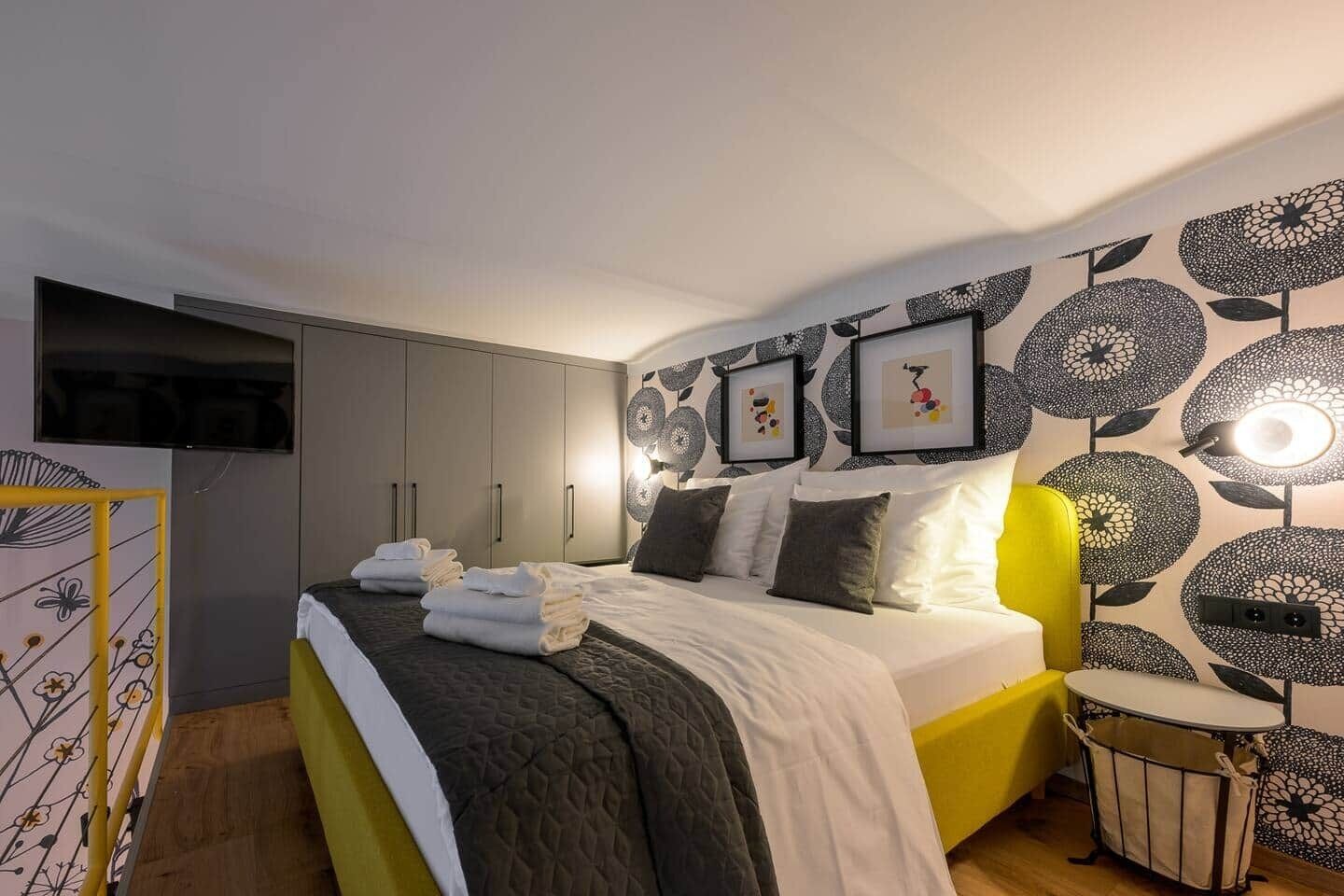 A bedroom with a bed, bedside tables, a wardrobe, and a wall with framed pictures.