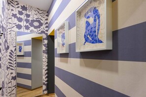 A hallway with striped walls and floral wallpaper, leading to a room with a bed. - IMCT - Dockhouse Soho 3 (Budapest)