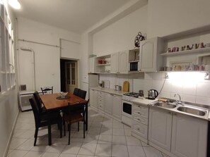 A compact kitchen with white cabinets, a dining table with chairs, a gas stove, and a sink. - IMCT - Elegance in the Heart (Budapest)