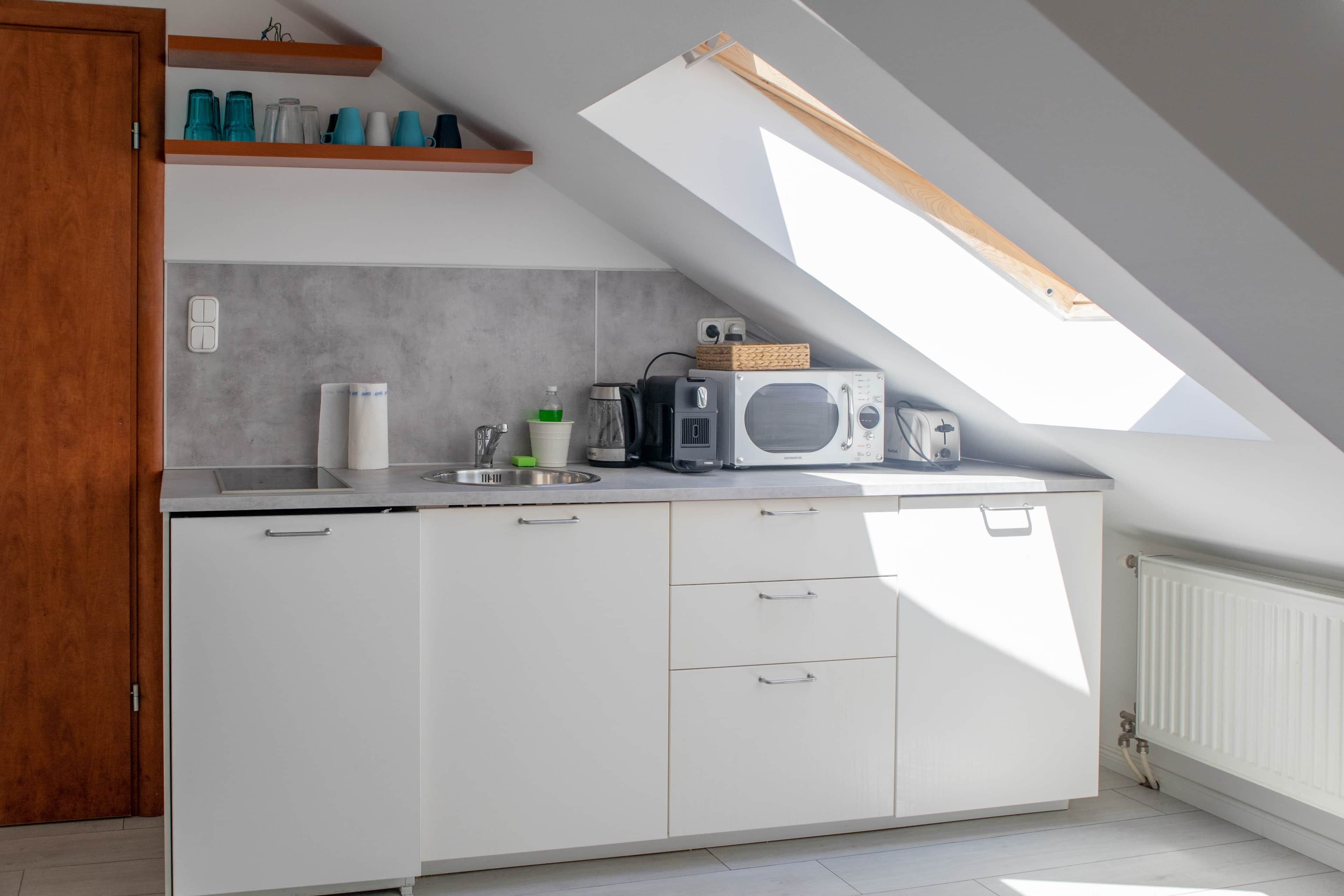 Een moderne keuken met een dakraam, witte kastjes en een inbouwmagnetron.