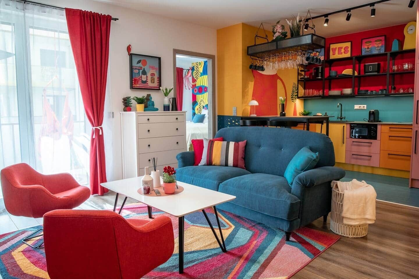 Una sala de estar moderna con un sofá azul, sillones rojos y una mesa de centro blanca.