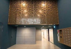 A hallway with a patterned wall, a large grey door, and a wall-mounted mailbox. - IMCT - FullBloom in the center (Budapest)