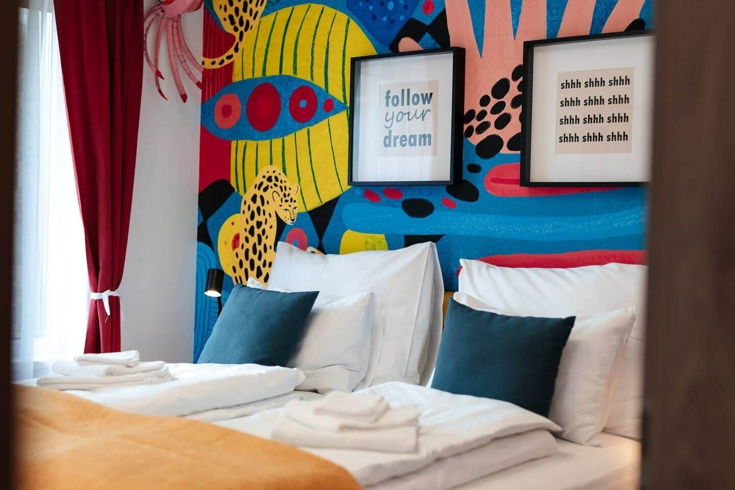 A hotel room with a bed, pillows, a wall with colorful artwork, and framed inspirational quotes.