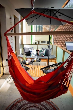 A room with a hanging chair, a sofa, a small table, and a view of the outside. - IMCT - FullBloom in the center (Budapest)