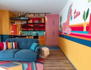 A modern living room with a sofa, a kitchen area, and a vibrant wall mural. - IMCT - FullBloom in the center (Budapest)