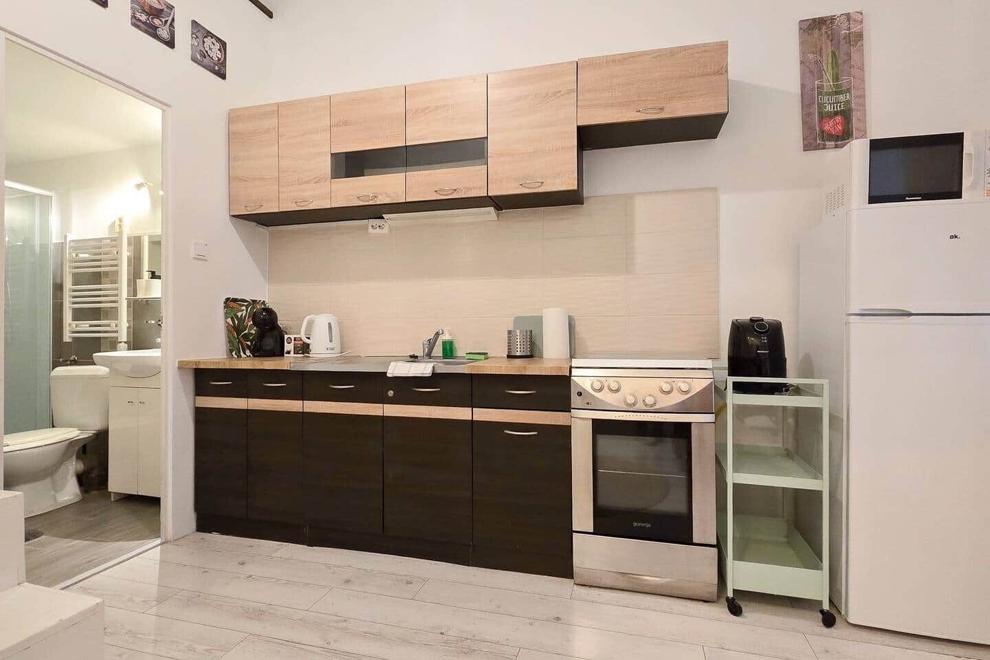 A compact kitchen with a stove, oven, and microwave, a small refrigerator, and a glass cabinet.