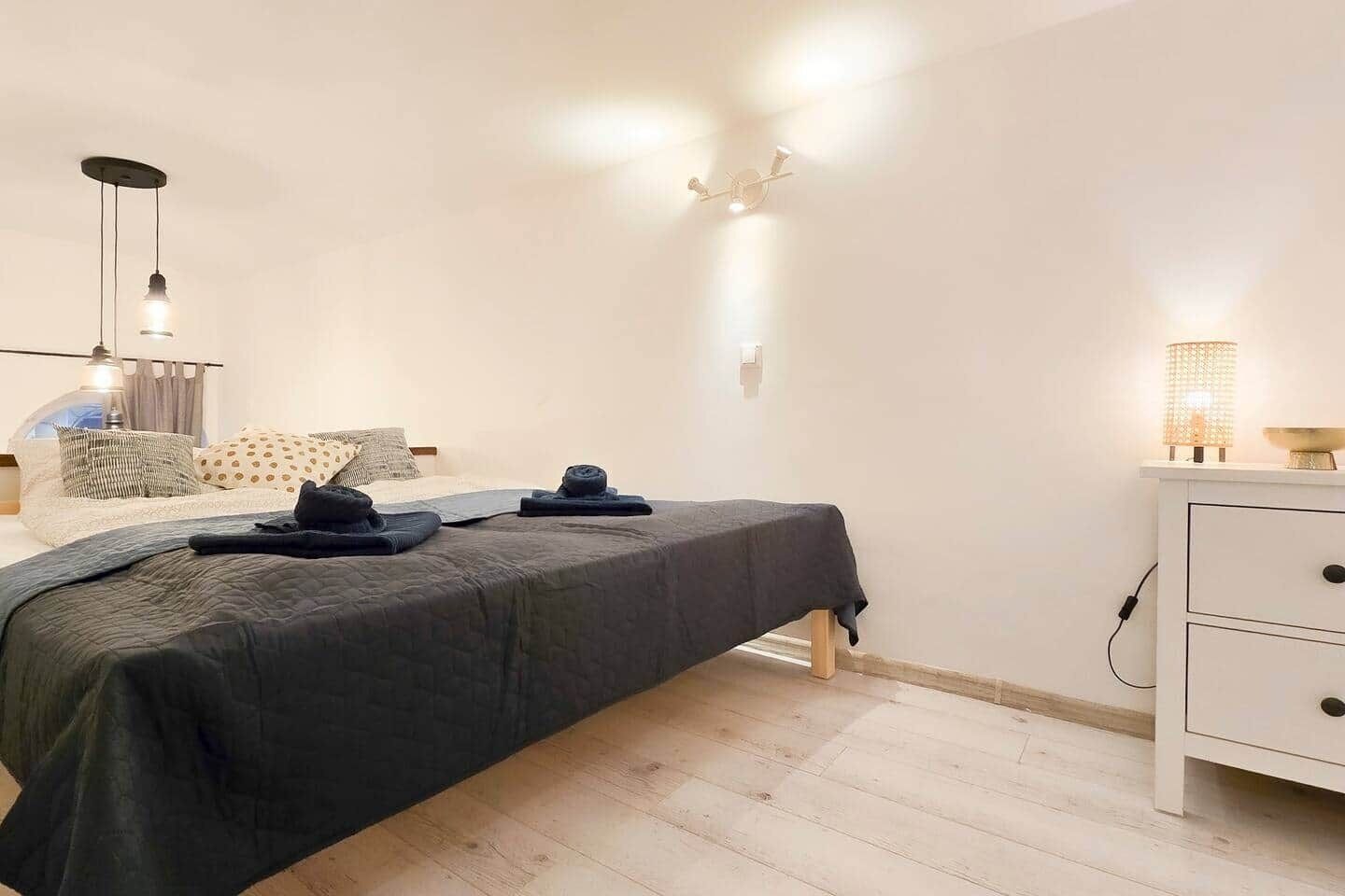 Une chambre à coucher comprenant un lit, une table de chevet, une lampe et un luminaire fixé au mur.