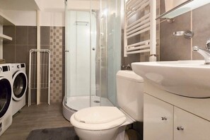 Ein Badezimmer mit einer Duschkabine, einer Toilette, einer Waschmaschine und einem Waschbecken.