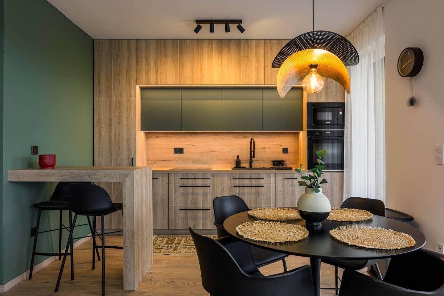 A modern kitchen with wooden cabinets, a black countertop, and a dining area with a round table and black chairs.