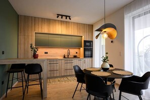 A modern kitchen with wooden cabinets, a black oven, and a dining area with a round table and black chairs. - IMCT - OpenSky Terrace with free parking (Budapest)