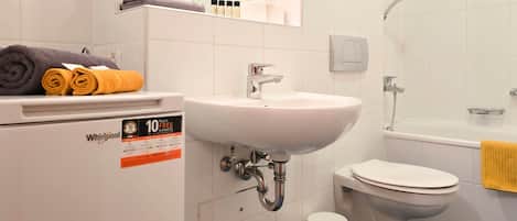 Un bagno con lavandino, WC e doccia. Asciugamani su uno scaffale e un cartello che indica una garanzia decennale.