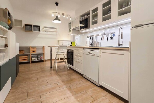 Una cucina moderna con mobili bianchi, lavastoviglie e un'area pranzo con una sedia e un tavolo.