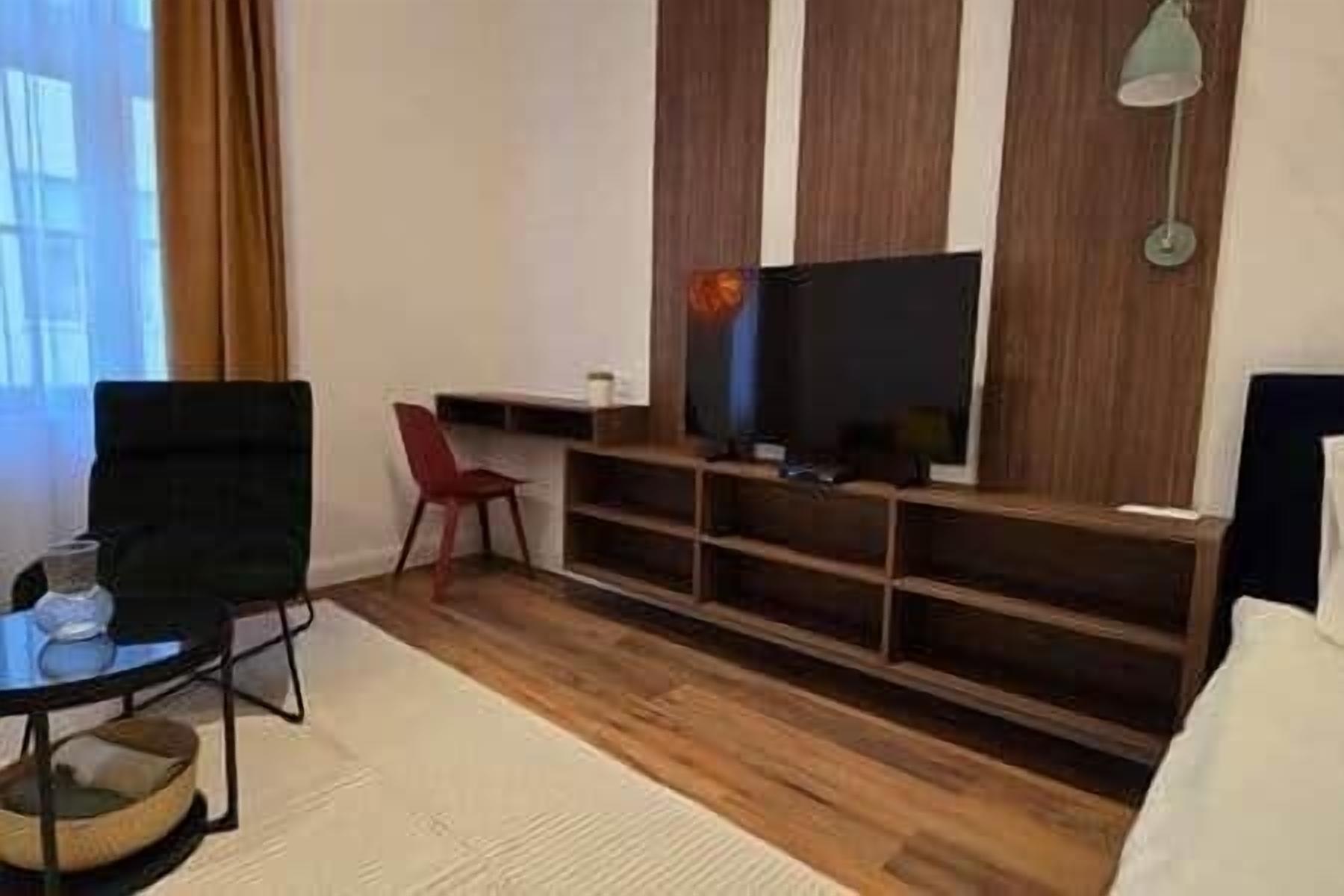 A room with a flat-screen TV, a red chair, a wooden TV stand, and a sofa.