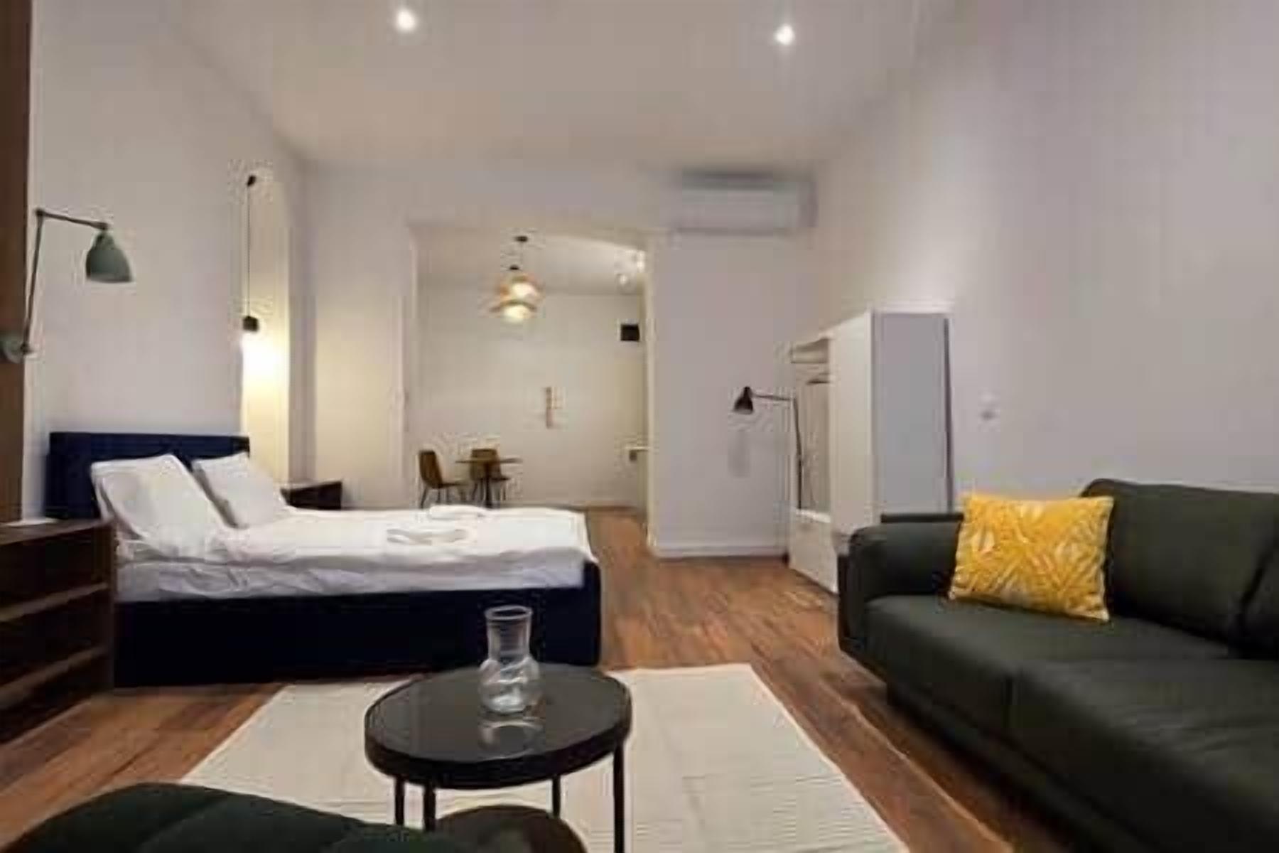 Un dormitorio moderno con cama, sofá, una mesita y un escritorio. Se ve una silla al fondo.