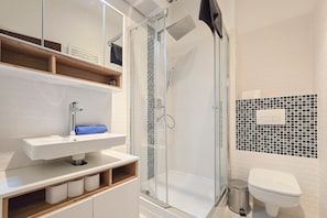 A modern bathroom with a glass-enclosed shower, a white sink, and a toilet. - IMCT - New City Life Apartment (Budapest)