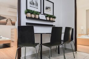 A modern room with a dining table, three chairs, a small shelf with plants, and framed pictures on the wall. - IMCT - New City Life Apartment (Budapest)