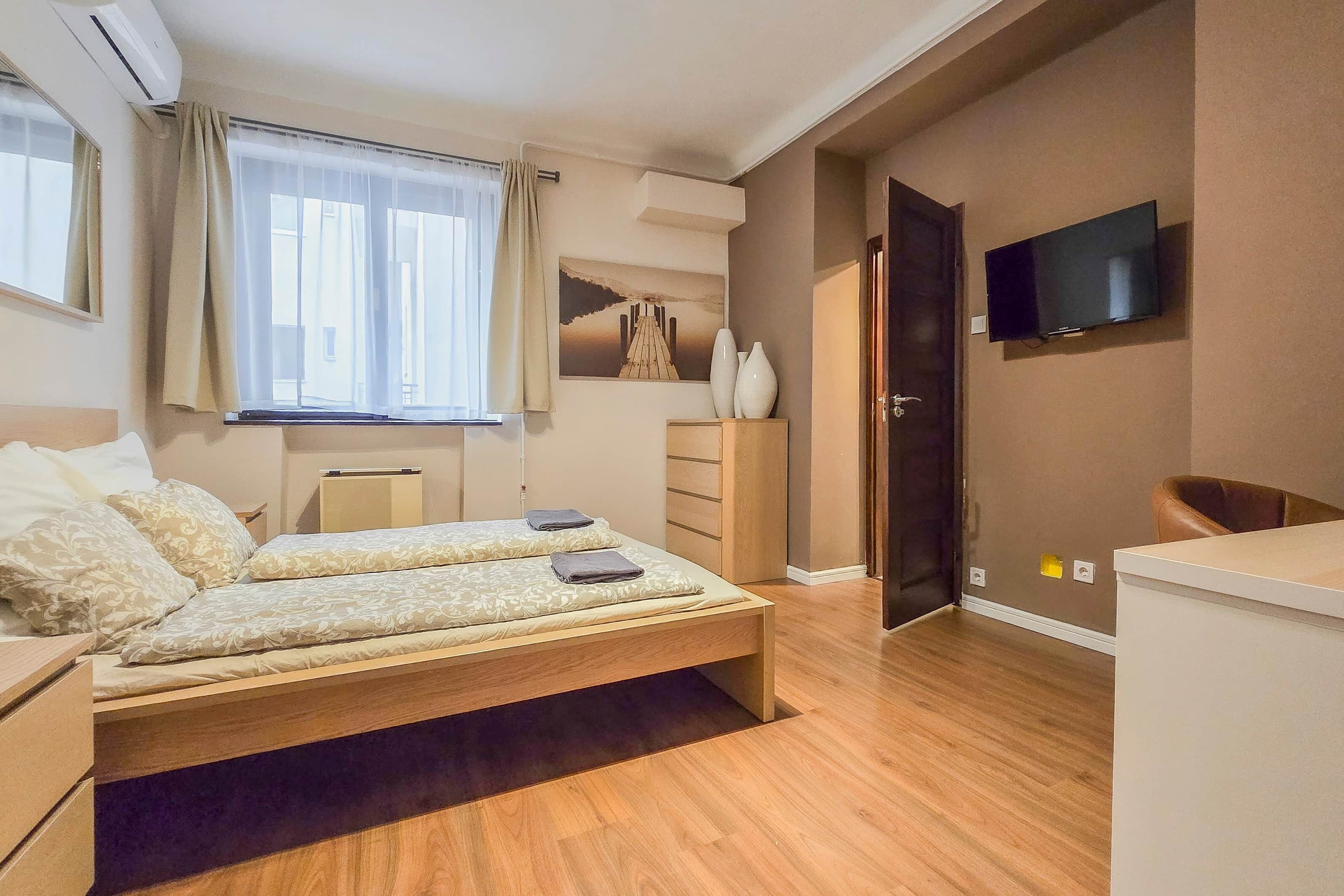 Une chambre à coucher comprenant un lit, des tables de chevet, une commode, un téléviseur et une fenêtre avec des rideaux.