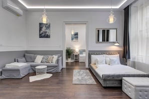 Een moderne slaapkamer met een grijze bank, een bed, een rond bijzettafeltje en een spiegel.