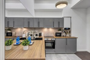 A modern kitchen with grey cabinets, a wooden countertop, and a built-in oven. - IMCT - Semmelweis Apartment A (Budapest)