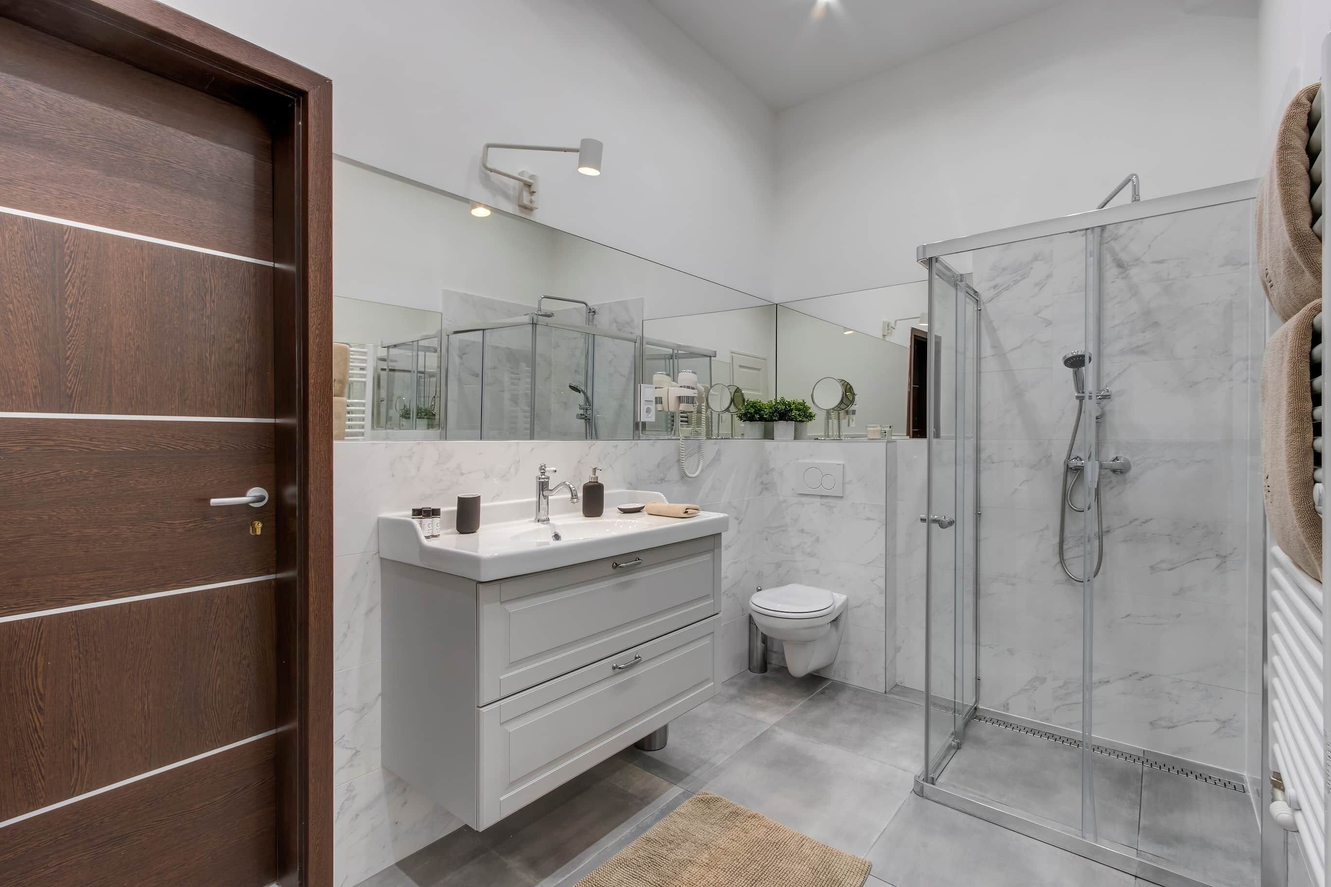 Ein modernes Badezimmer mit Holztür, Waschtisch mit Spiegel, Dusche und Toilette.