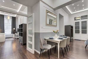 A modern dining area with a white table, grey chairs, and a mirror above. - IMCT - Semmelweis Apartment A (Budapest)