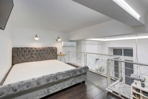 Ein Schlafzimmer mit einer gesteppten Kopfteil, einem Bett, einem kleinen Nachttisch und einem Balkon mit Geländer.
