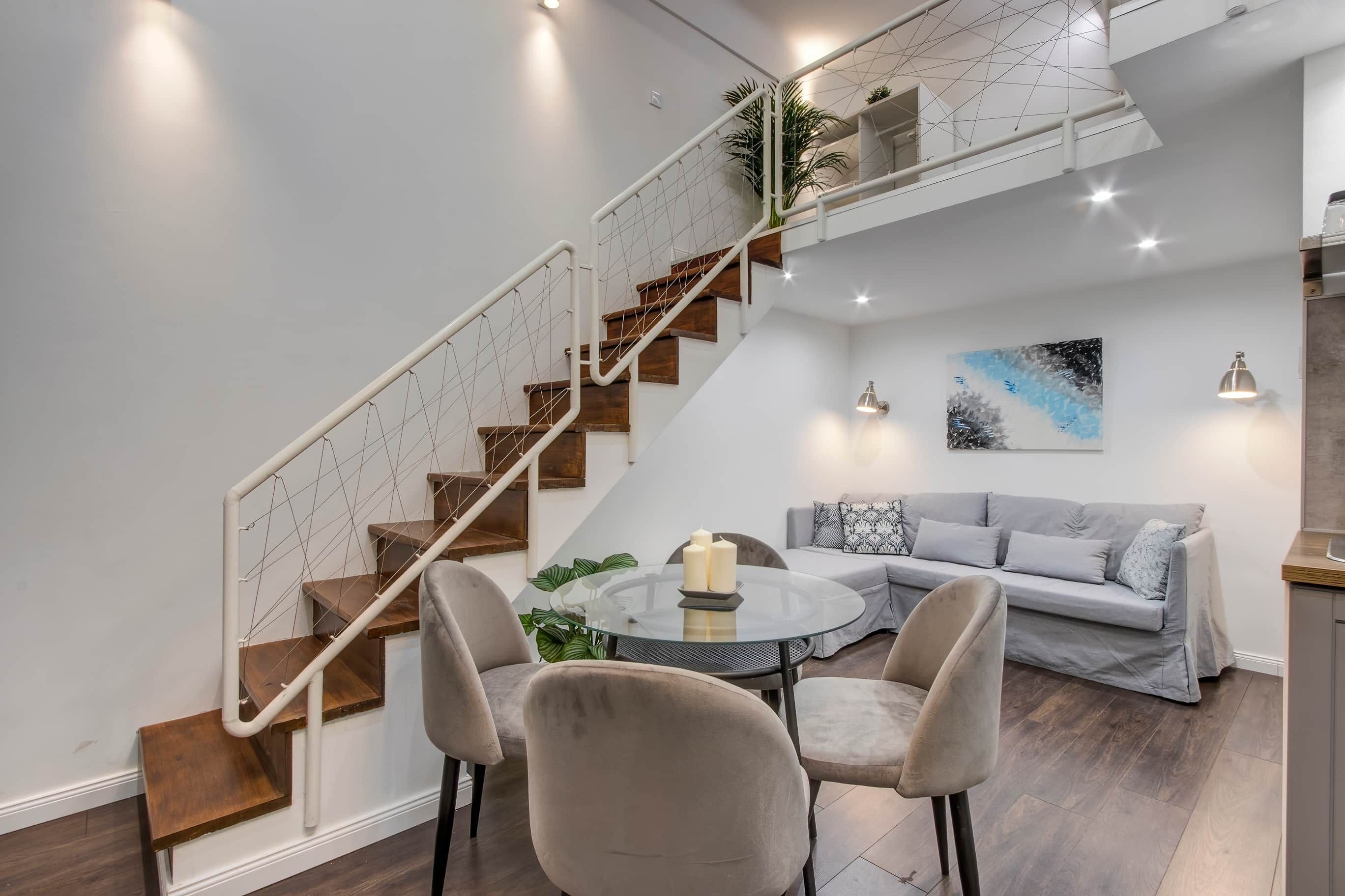 Et moderne interiør med en trappe, et rundt glasbord og en grå sofa.