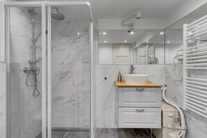 Ein modernes Badezimmer mit einer gläsernen Dusche, einem Marmorboden, einem Holzkosmetikschrank mit Waschbecken und einem großen Spiegel.