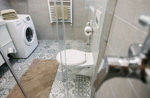 A compact bathroom with a washing machine, toilet, and shower. - IMCT - Tailor Apartment in the Center (Budapest)