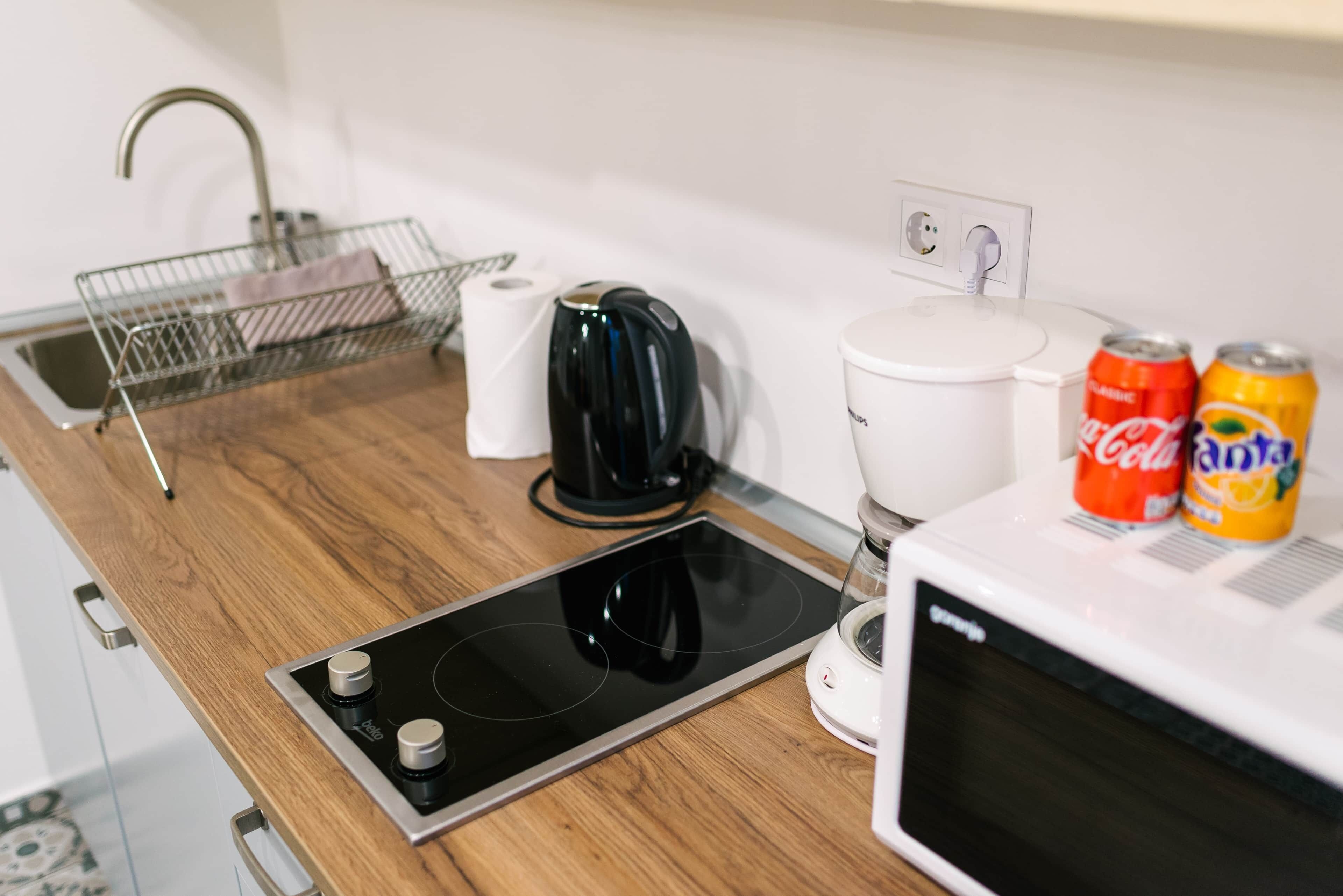 A kitchenette with a stove, kettle, microwave, and a coffee maker.