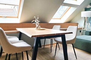 A dining area with a wooden table and four chairs, a vase with flowers, and a view of the sky through skylights. - IMCT - Urban Jungle Apartments 05 (Budapest)