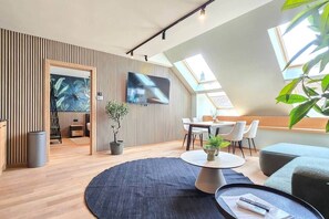 A modern living room with a flat-screen TV, a dining area, and a large window with natural light. - IMCT - Urban Jungle Apartments 05 (Budapest)