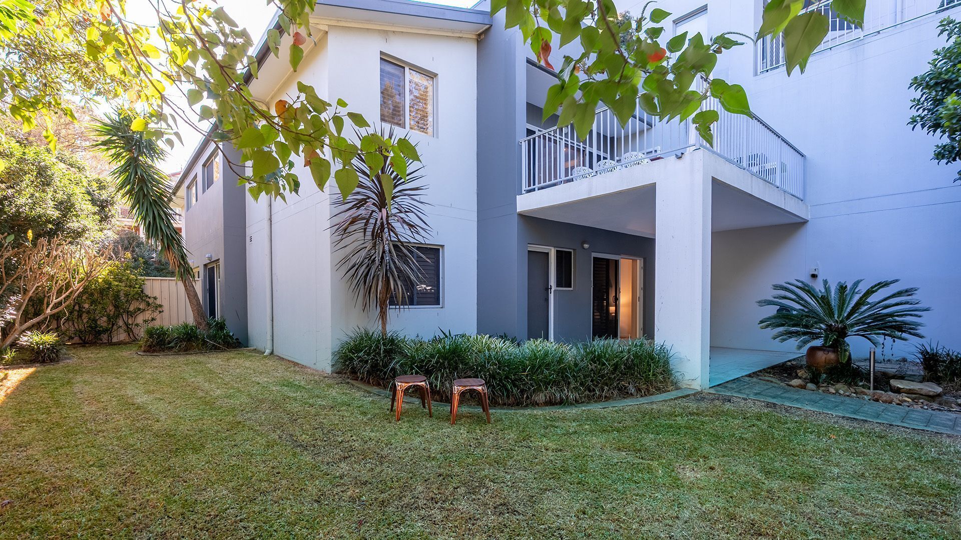 A modern two-story building with a flat roof, a balcony, and a well-maintained lawn.