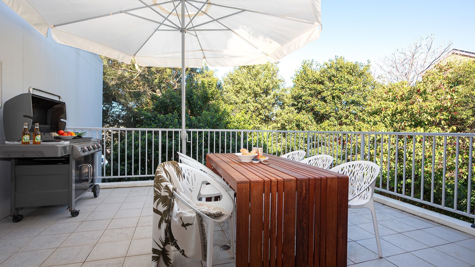 An outdoor patio with a grill, dining table, chairs, and an umbrella.