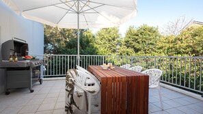 An outdoor patio with a grill, dining table, chairs, and an umbrella.