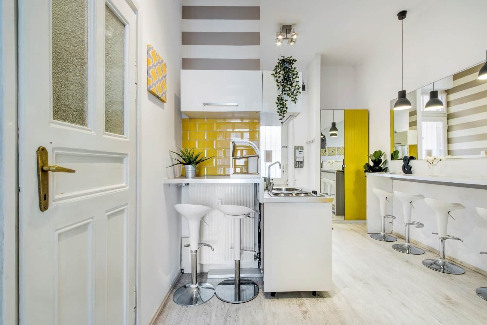 Une cuisine moderne avec des carreaux blancs et jaunes, un îlot central doté de tabourets et un coin bar également équipé de tabourets.