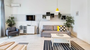 Ett modernt vardagsrum med en soffa, ett soffbord, en tv och en gul hänglampa.