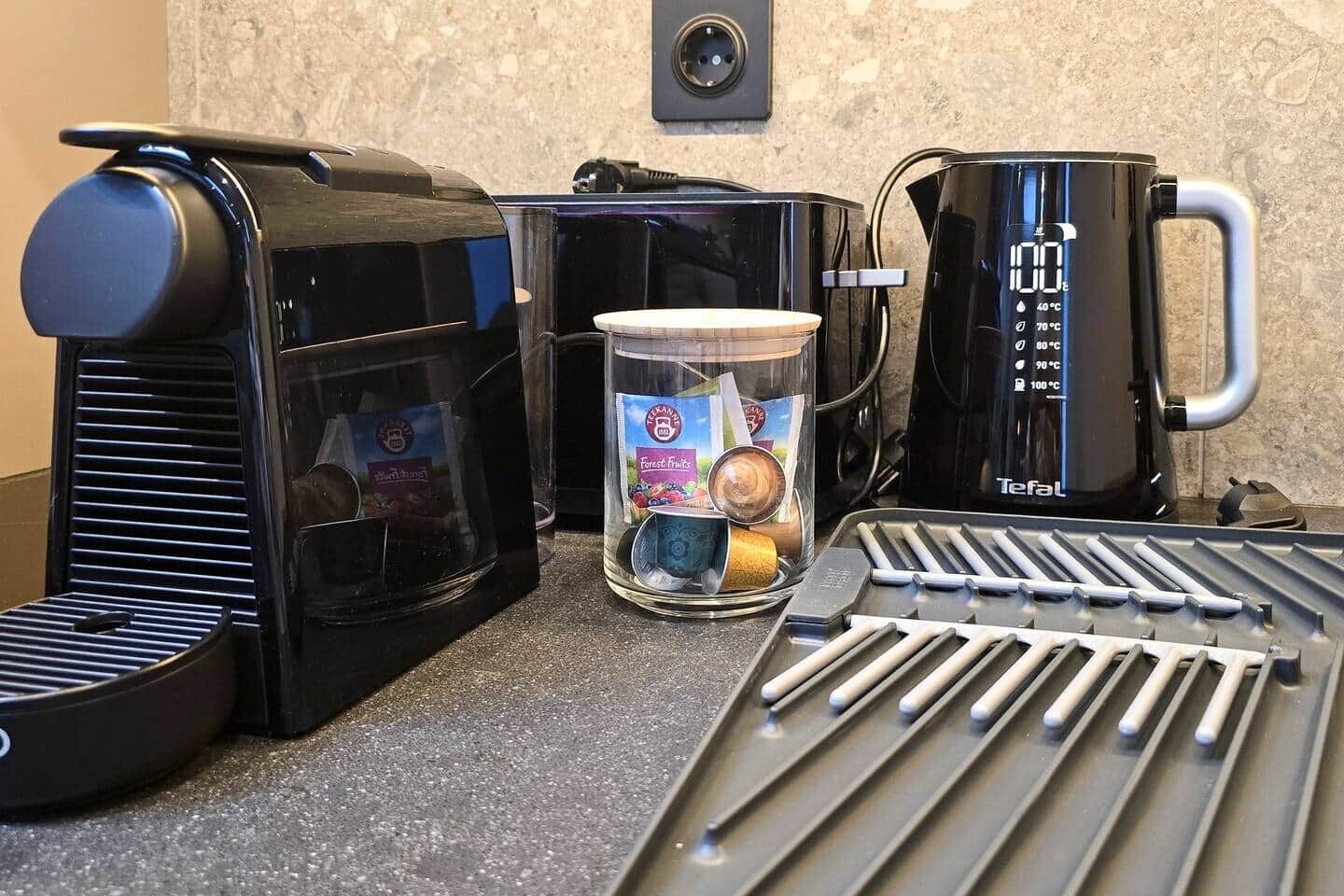 Uma cozinha com cafeteira, chá em sachês e um suporte com utensílios.