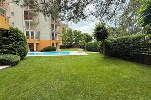A residential area with a swimming pool, a well-maintained lawn, and a multi-story building with balconies. - LB - Balaton Nova Apartment-Beachfront (Siófok)