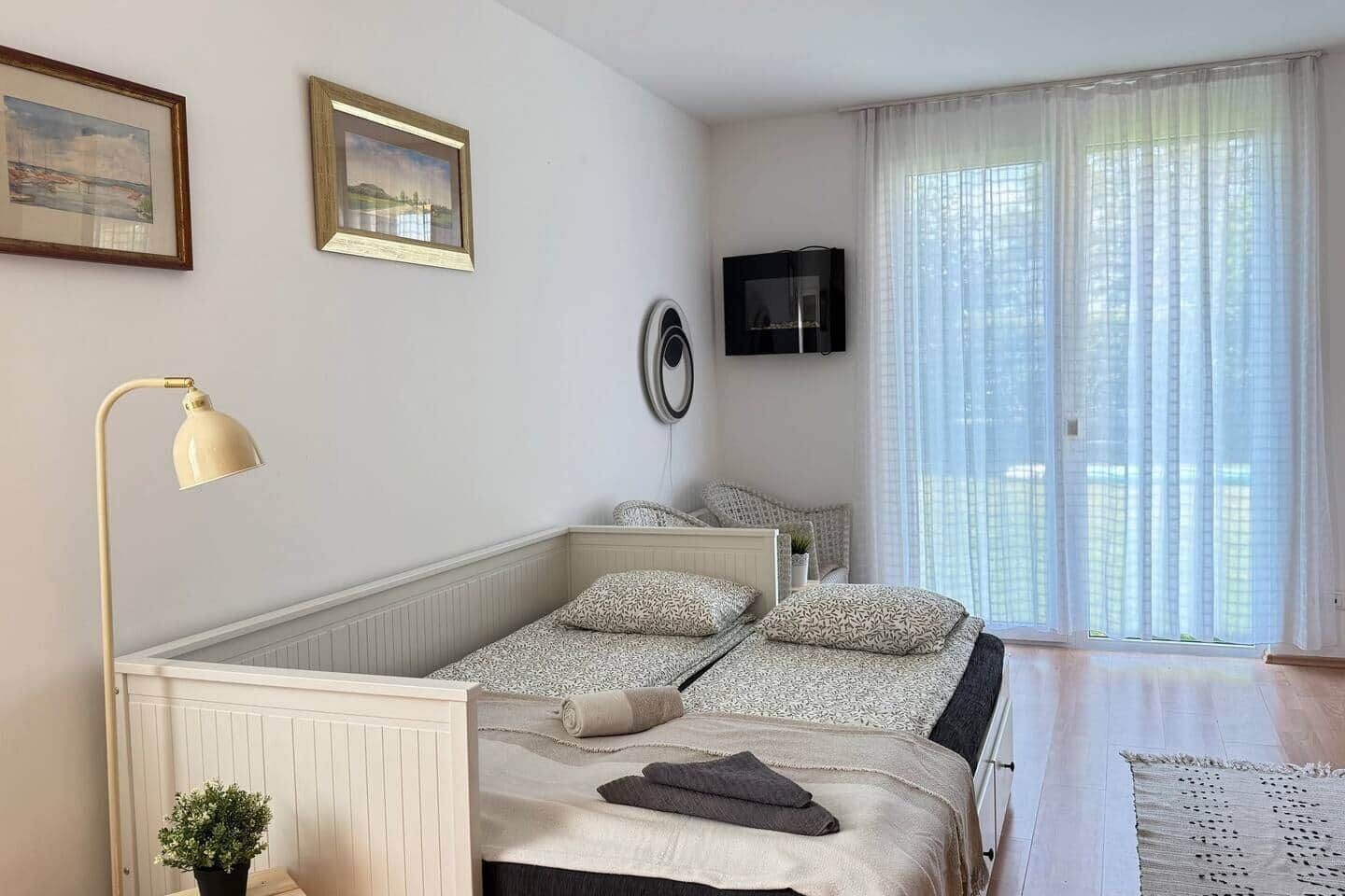 Une chambre à coucher avec un lit, une lampe de chevet, une télévision et une fenêtre avec des rideaux.