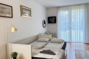 Un dormitorio con una cama, una lámpara de noche, un televisor y una ventana con cortinas.