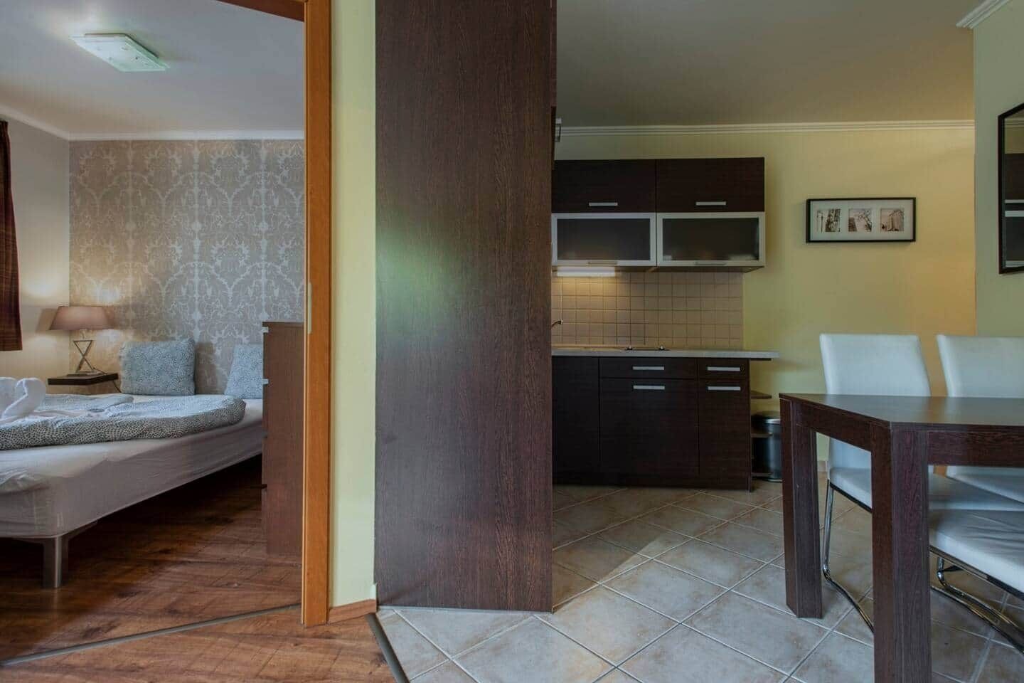 A modern living room with a sofa, a dining table, and a kitchen area with cabinets and a tiled backsplash.