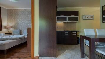 A modern living room with a sofa, a dining table, and a kitchen area with cabinets and a tiled backsplash.