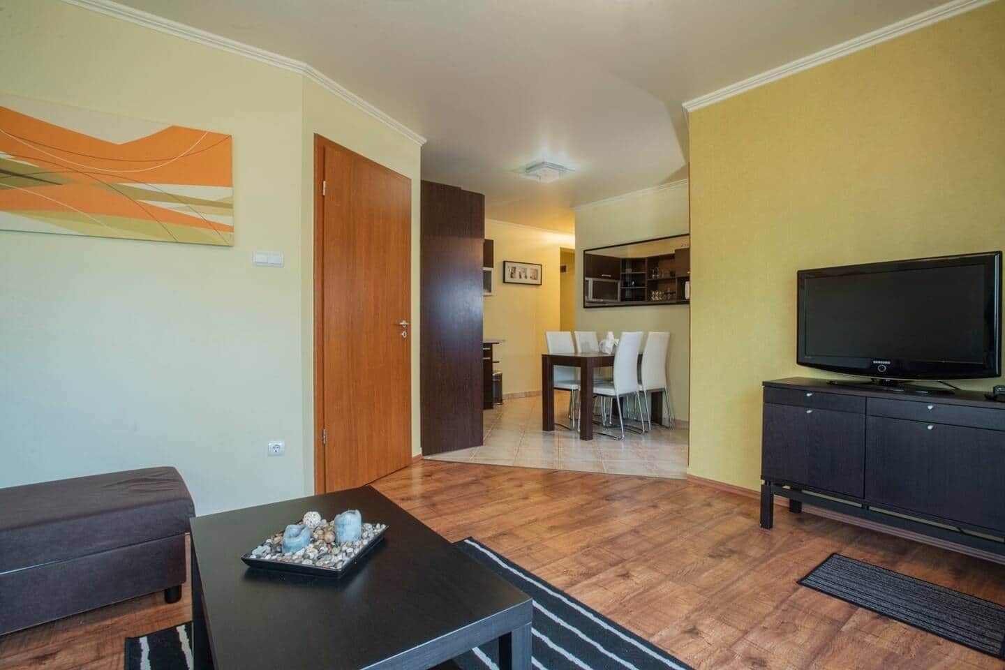 A living room with a dining area, a TV, and a kitchen in the background.