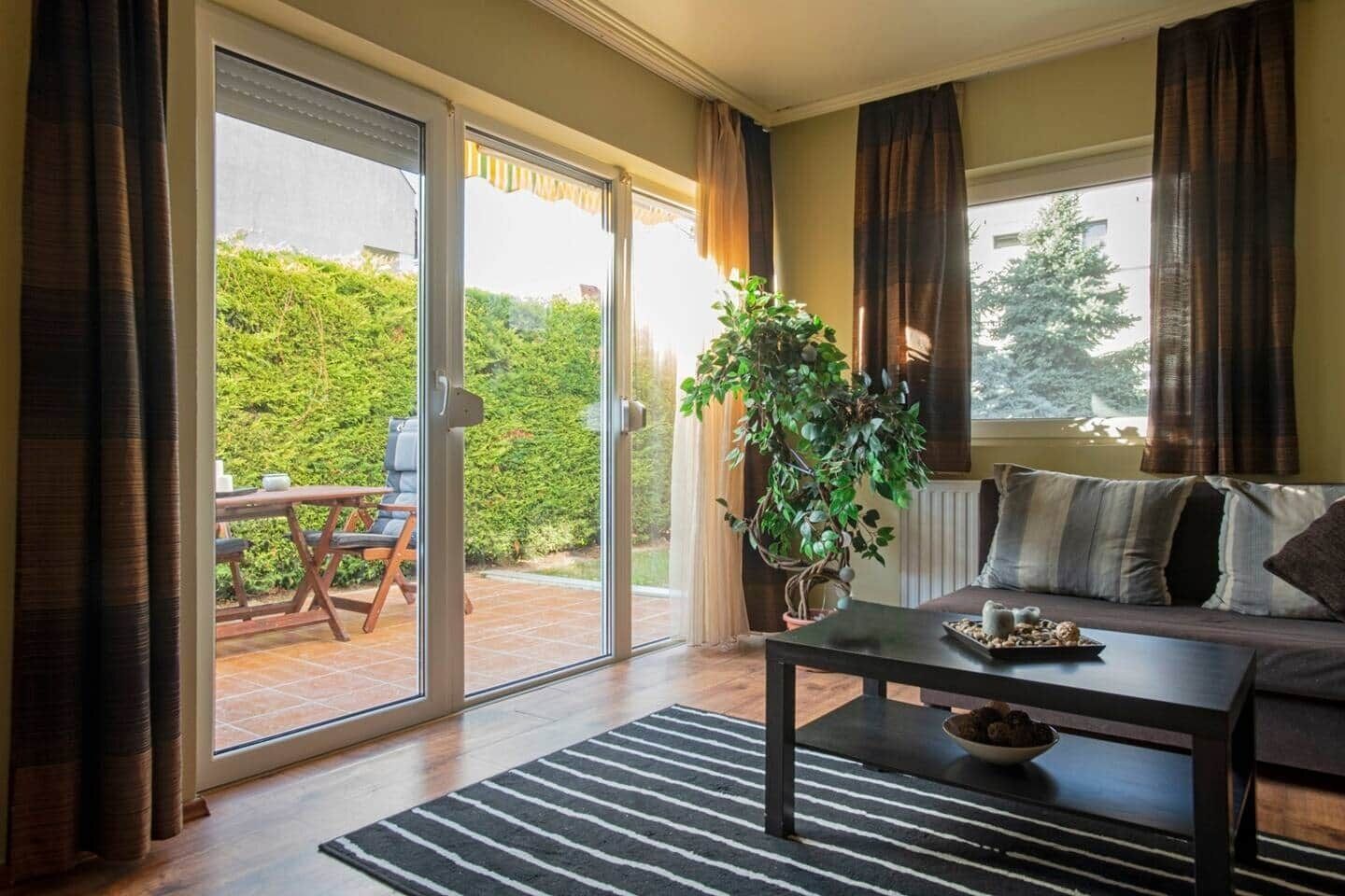 A living room with a sofa, a coffee table, a potted plant, and a sliding glass door leading to an outdoor area with a table and chairs.