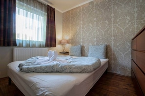 Una habitación de hotel con cama, mesita de noche, lámpara y ventana con cortinas.